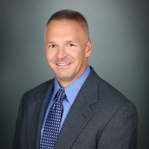 Brian Smith, M.D., a man with short, grey hair, wearing a grey patterned suit.