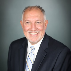 Carlos Santos, M.D., a man with grey hair and a beard, wearing a black suit