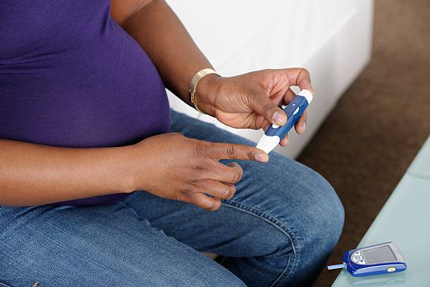 A close-up of a pregnant African American woman monitoring her blood glucose/ sugar at home to be aware of gestational diabetes.