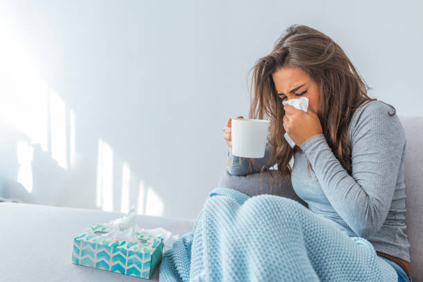 a patient sitting on the couch suffering from flu symptoms because she did not get a flu shot. 